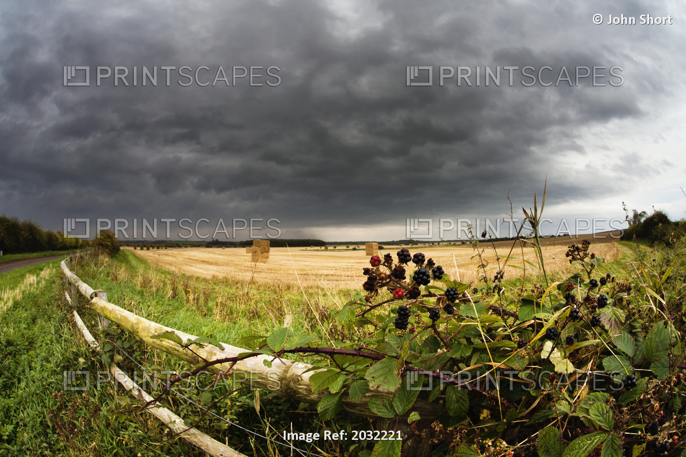 A Wooden Rail Fence Along The Edge Of A Farm Field Under Storm Clouds; ...