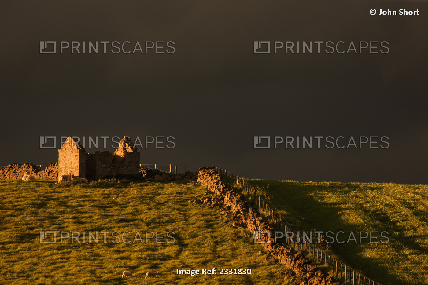Dark storm clouds over building ruins and a stone fence along a field at ...
