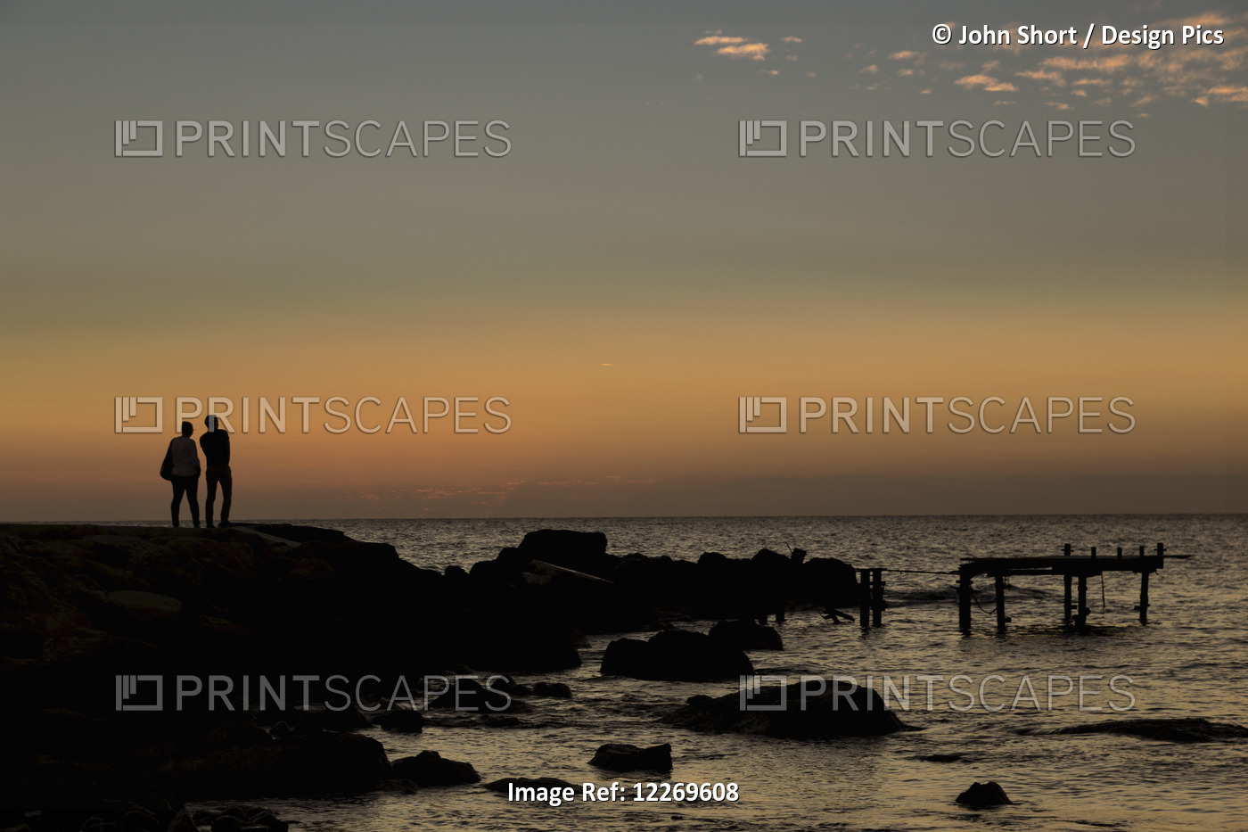 Silhouette Of Two People Standing At The Water's Edge Watching The Sunset Over ...