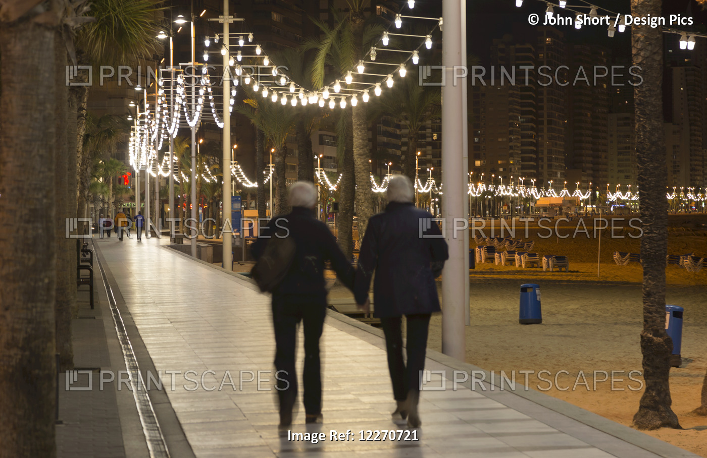 A Couple Walking And Holding Hands Along A Promenade On The Beach; Benidorm, ...