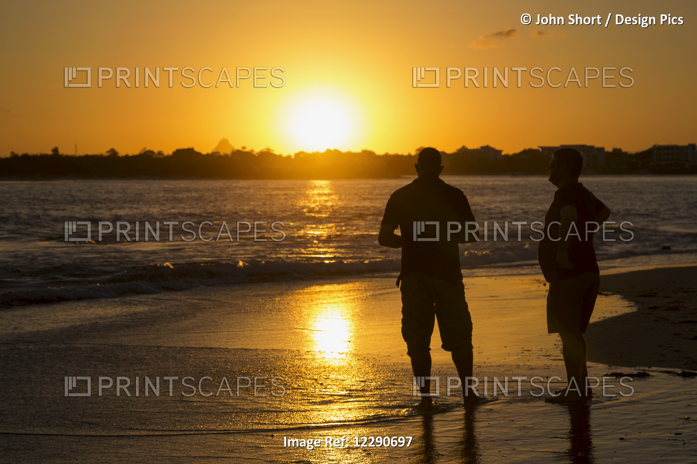 Two Men Stand In The Tide Water On A Beach At Sunset; Caloundra, Queensland, ...
