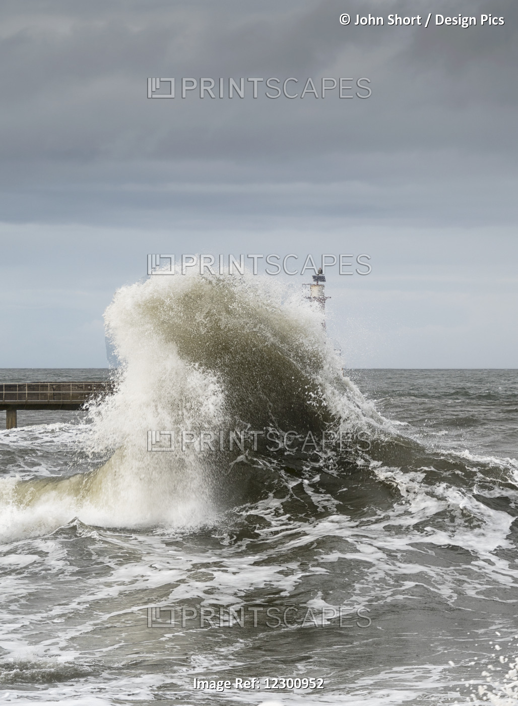 Large Wave Crashing At The Coast With A Lighthouse At The End Of A Pier; Amble, ...