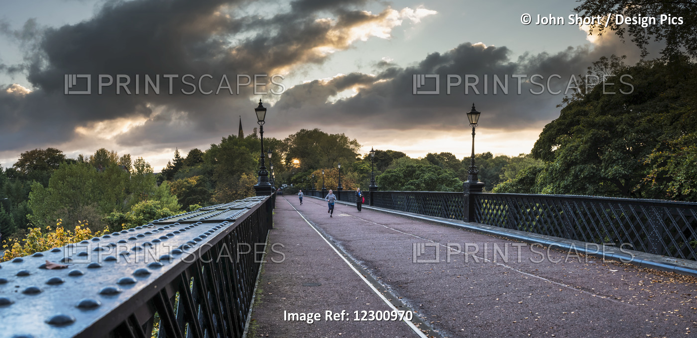 Pedestrians And A Runner On A Bridge With Clouds Glowing At Sunset; Newcastle, ...