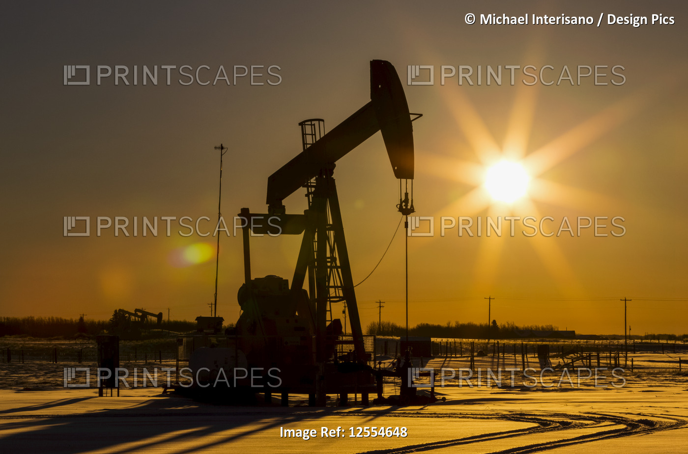Silhouette of pumpjack in snow-covered area with an orange starburst sun at ...