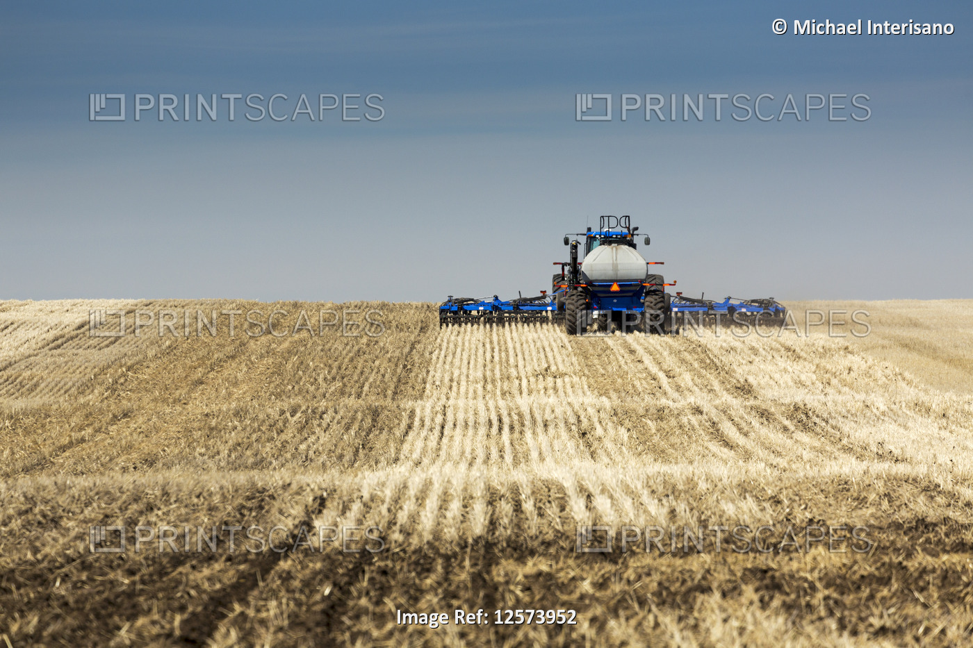 Back view of air seeder, seeding a stubble field with blue sky and hazy clouds, ...
