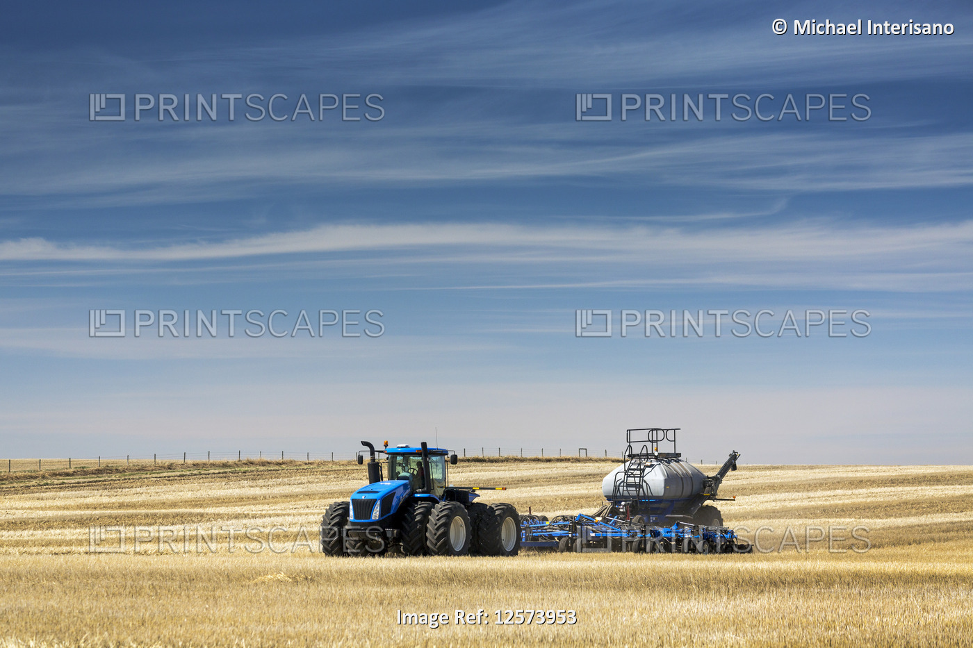 Tractor with air seeder, seeding a stubble field with blue sky and hazy clouds, ...