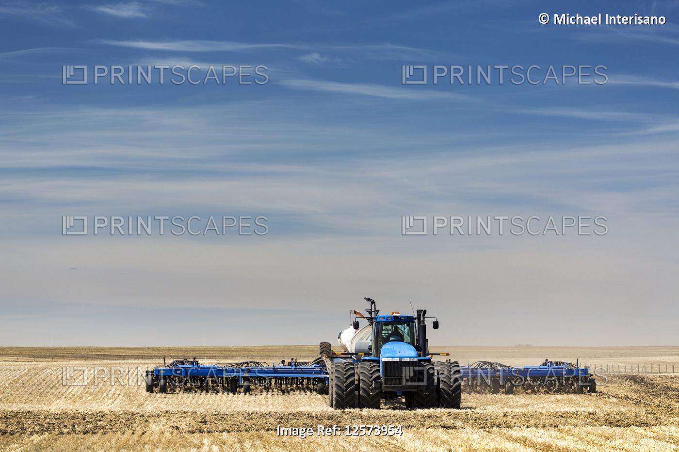Tractor with air seeder, seeding a stubble field with blue sky and hazy clouds, ...