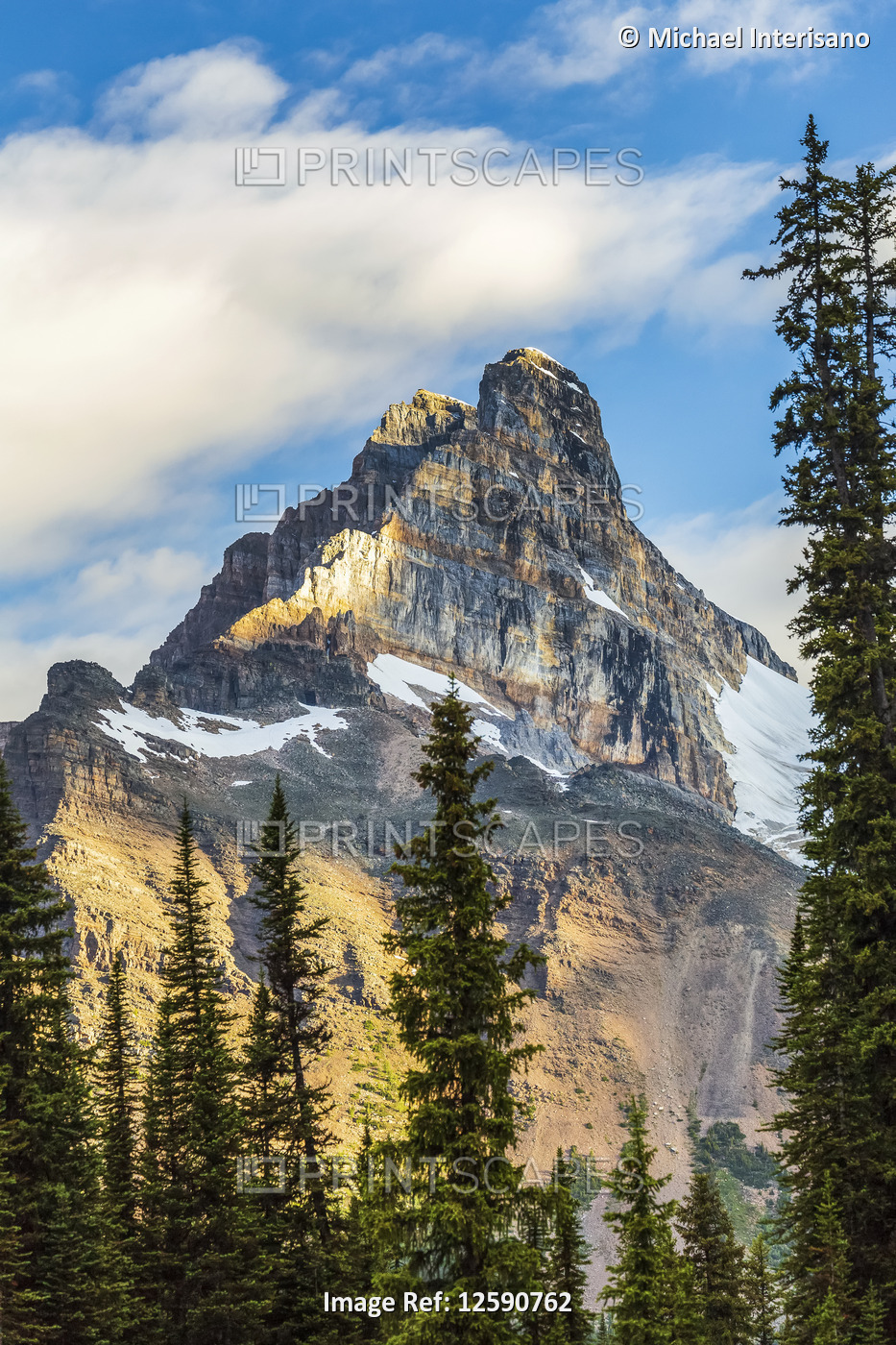 Mountain cliff peak dramatically lit by the sun with blue sky and clouds, Yoho ...