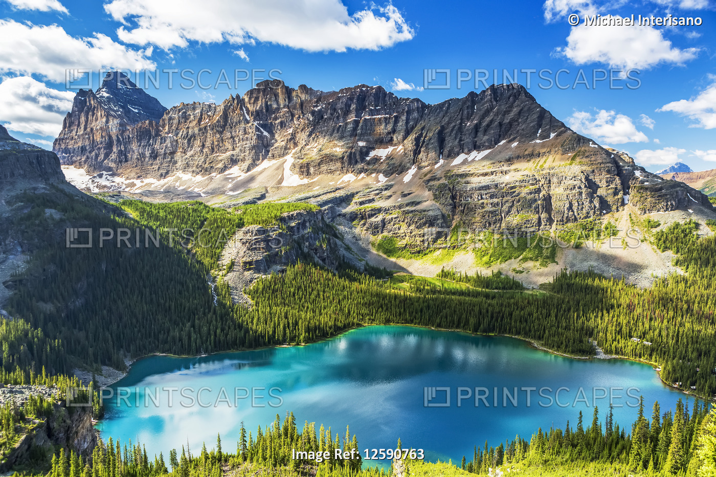Beautiful blue alpine lake with rugged mountain in the distance with blue sky ...