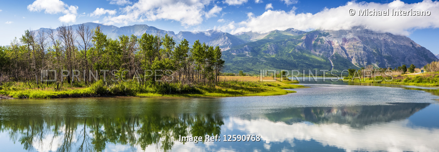 Panorama of mountain scape and tree island reflecting off a still lake with ...