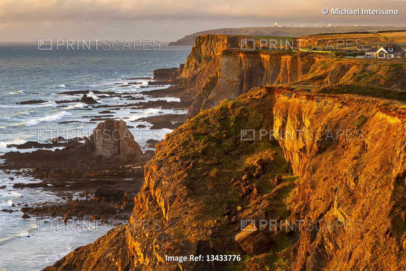 Dramatic rocky cliffs along the shoreline with the orange glow of sunset; ...