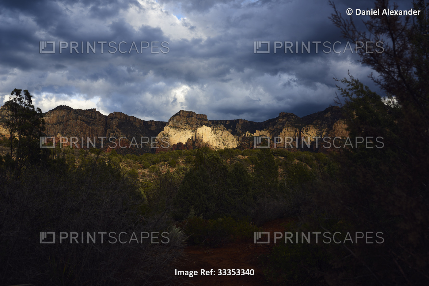 Gathering storm clouds and dramatic light on red rock mountains with forest in ...