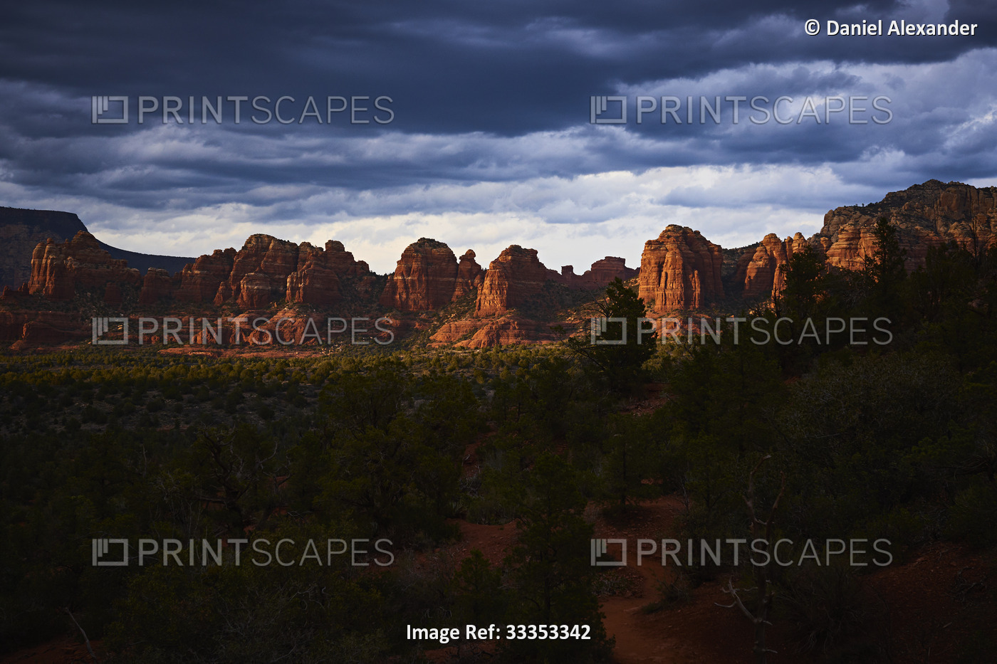 Dramatic sunset landscape of red rock formations with scrub and forest in the ...